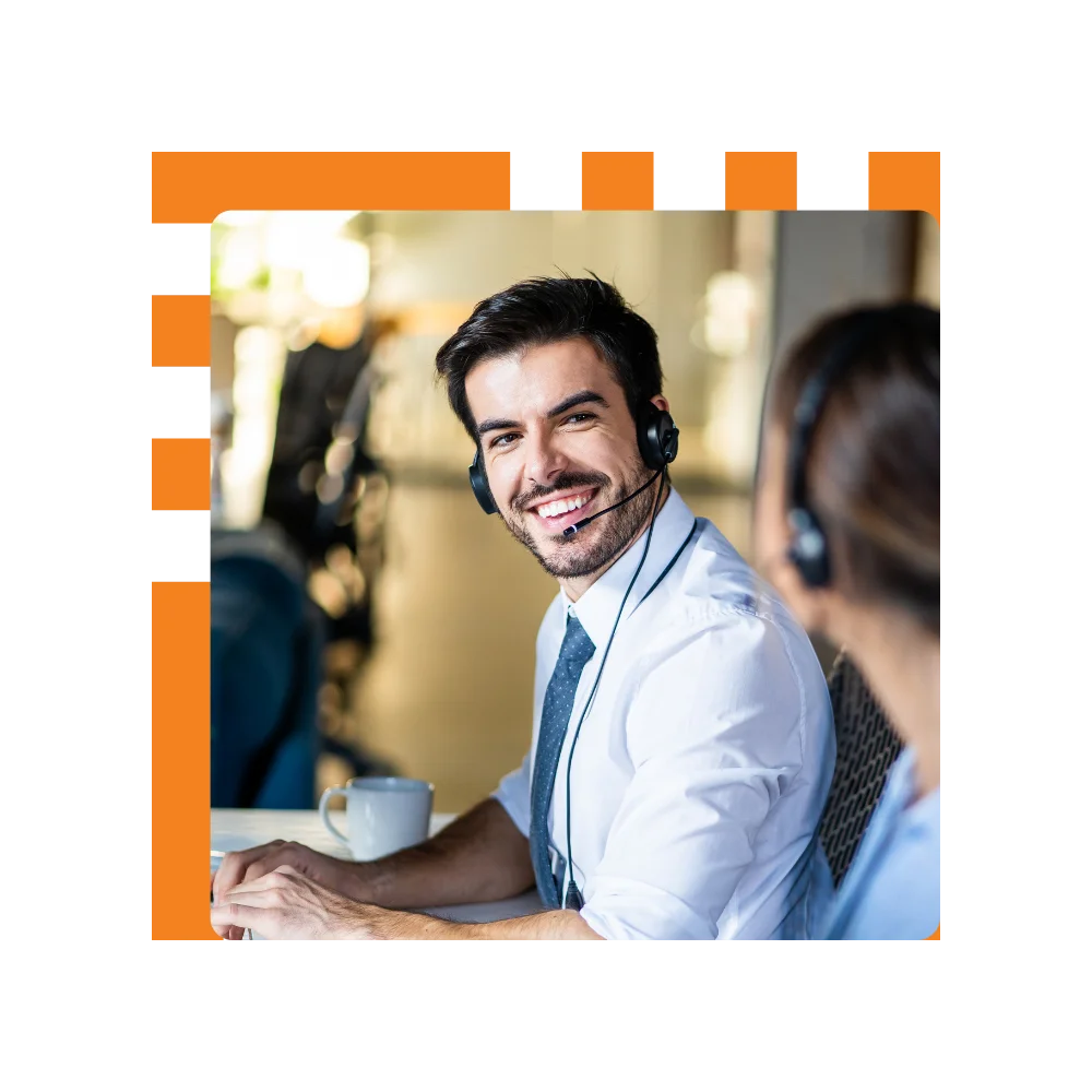 A smiling man wearing a headset sits at a desk, engaged in conversation or work, exuding a positive demeanor